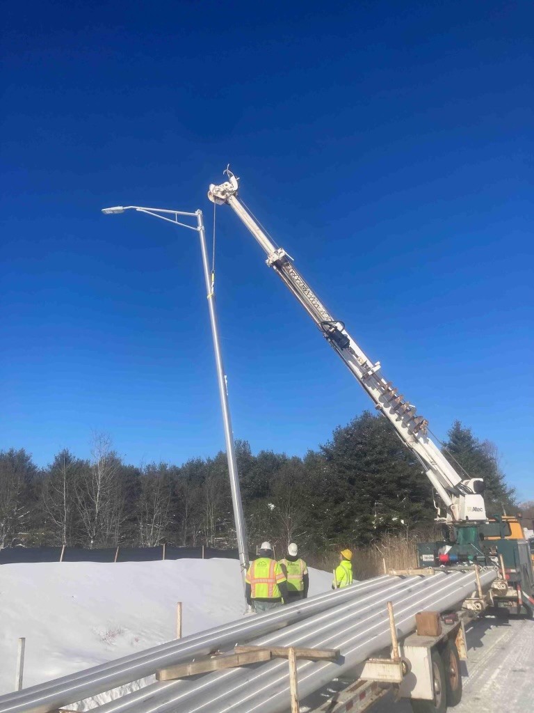 A crane raising a light post on the side of a highway